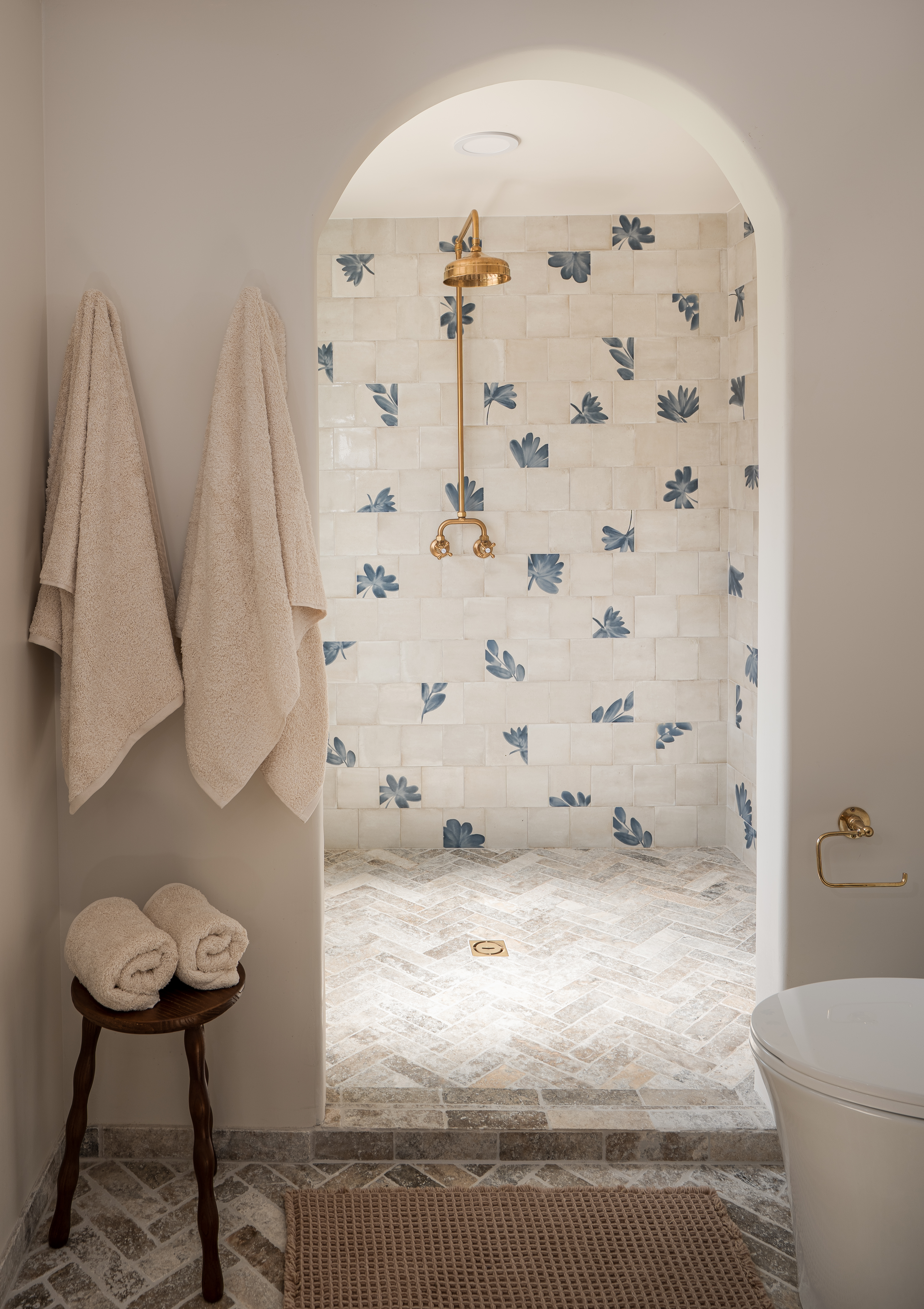 Arched walk-in shower with mixed floral zellige tile and travertine floors in Palm Springs primary bathroom