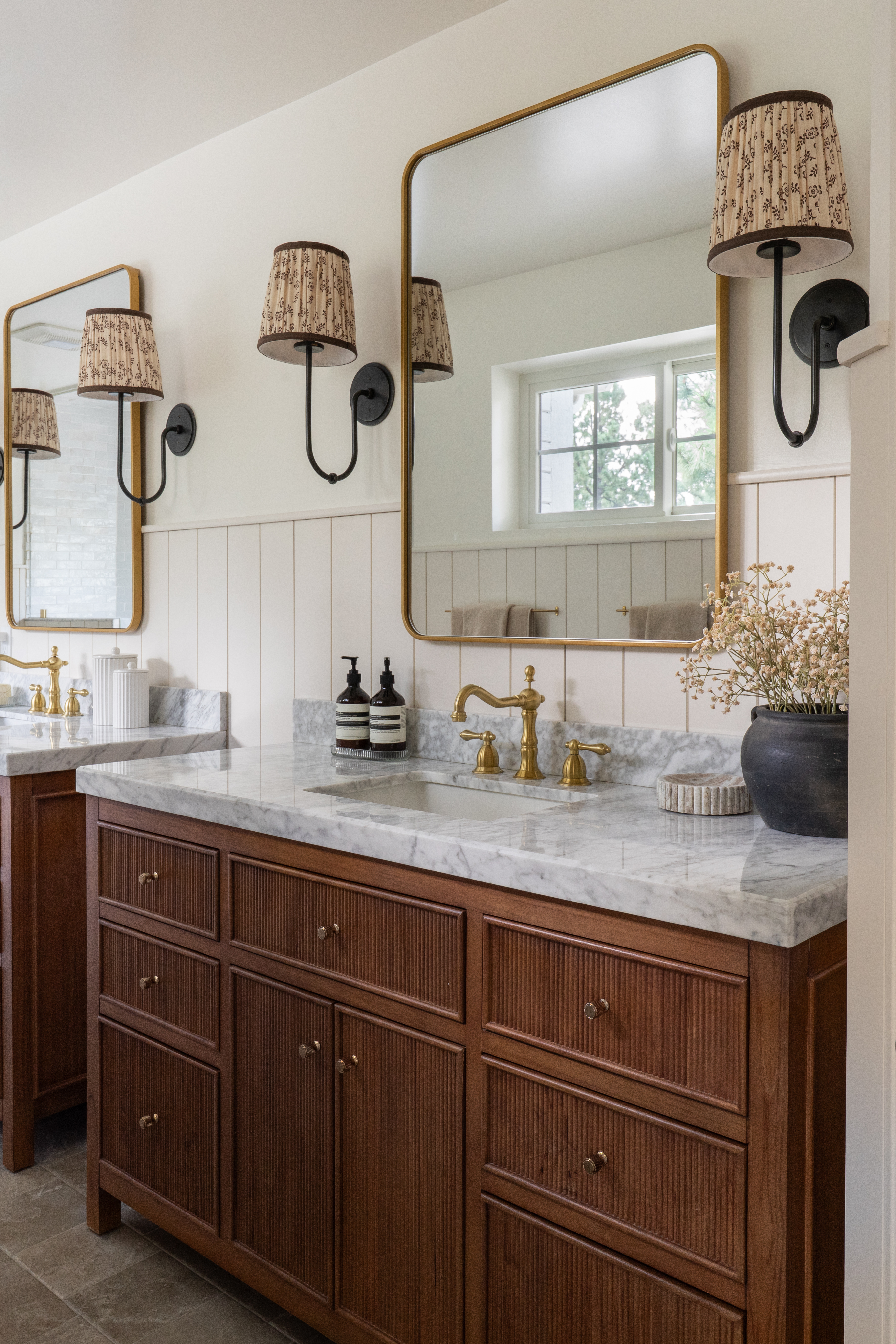 Double fluted wood vanities with marble counters and brass fixtures in Castle Pines primary bathroom